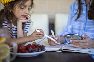 Focused mother and daughter looking paper schedule notebook together relaxing at outdoor terrace