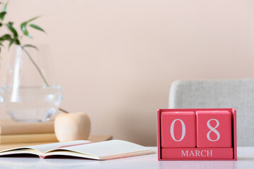 Cube calendar with date MARCH 8 and notebook on table in room