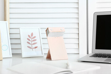 Tear-off calendar, frames and laptop on table in room