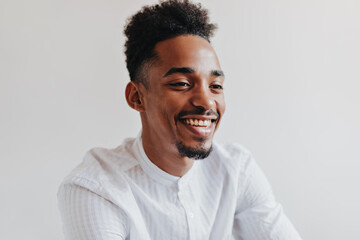 Obraz premium Optimistic man smiling on isolated background. Cool brunette man in white shirt laughing. Portrait of dark-skinned guy