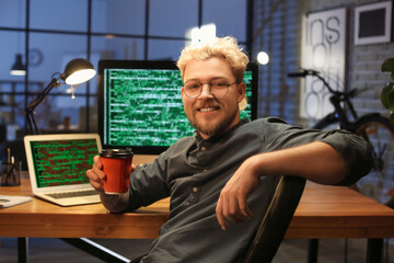 Young programmer drinking coffee in office at night
