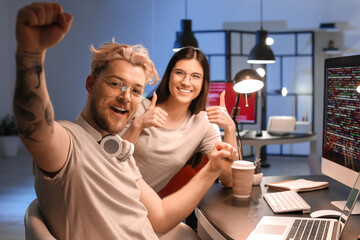 Happy young programmers working in office at night - obrazy, fototapety, plakaty