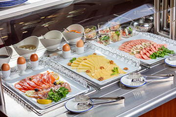 Slicing fish, cheese, sausage with meat on white trays.