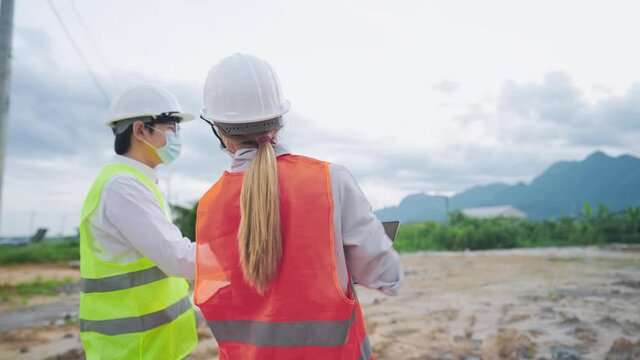 Asian Civil Engineer worker, architectural investor wear safety vest and hard hat discussing on the working project at construction land site, specialist job, Real Estate builder planning detail