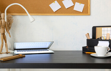 Modern workplace with laptop near light wall