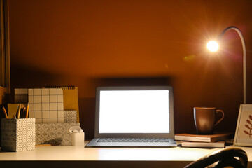 Modern workplace with laptop and glowing lamp in dark room