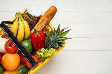 Shopping basket with food on white wooden background