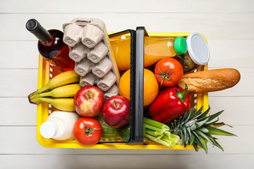 Shopping basket with food on white wooden background