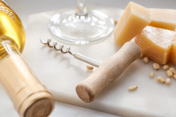 Board with bottle of exquisite wine, cheese and corkscrew on light table, closeup