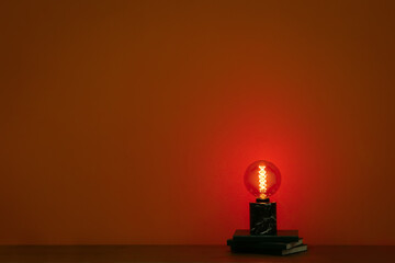 Glowing lamp and books on table in dark room