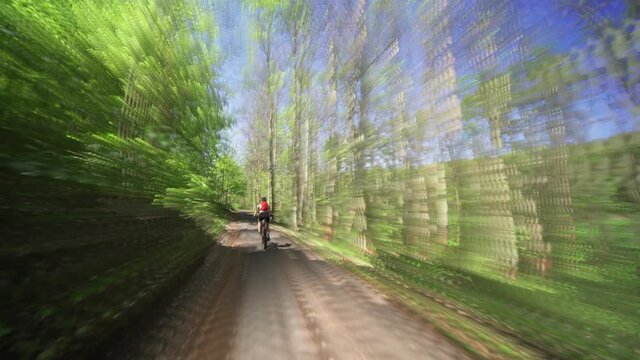 The back view of the female cyclist riding a bicycle on an asphalt road in the Divoka Sarka natural park in Prague on a summer day.