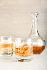 Jug and glasses of cold whiskey on light background