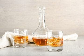 Jug and glasses of cold whiskey on light background