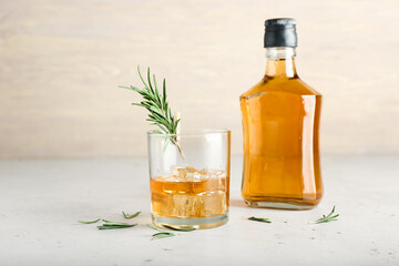 Bottle and glass of cold whiskey on light background