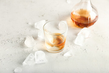 Jug and glass of cold whiskey on light background