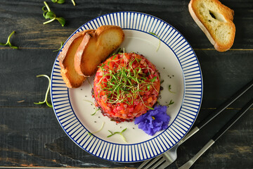 Plate with tasty tartare salad, toasted bread and flower on dark wooden background