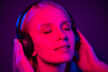 Happy young woman in black headphones with closed eyes in neon light. Red, blue and purple lights illuminate her face. The concept of night clubs and discos. Close-up.