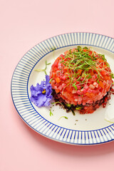 Plate with tasty tartare salad and flower on color background