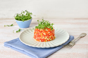 Plate with tasty tartare salad on light wooden background