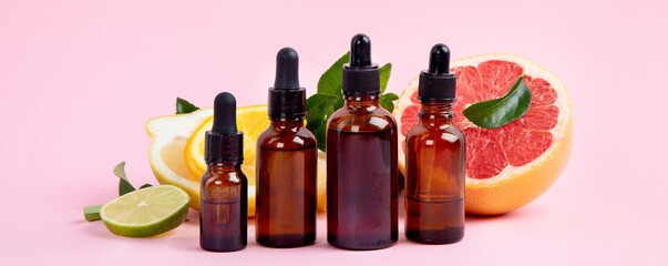 Bottles of essential aroma oils with citrus on pink background.