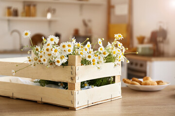Box with chamomiles on table in kitchen, closeup