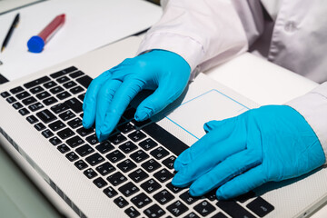 The doctor's hands in medical gloves lie on the keyboard. The doctor is typing text on the computer. A medical worker writes out a sick leave electronically. Close-up