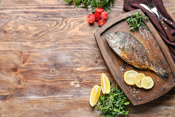 Board with fried dorado on wooden background
