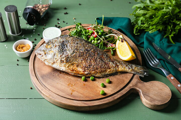 Board with fried dorado on color wooden background