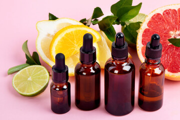 Bottles of essential aroma oils with citrus on pink background.