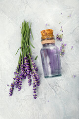 Bottle of essential oil and lavender flowers on light gray background.