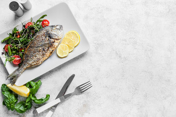 Plate with fried dorado and salad on light background