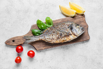 Wooden board with fried dorado on light background