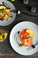 Plates with tasty tomato carpaccio and oil on dark wooden background
