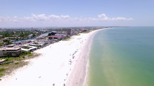 Drone shot of Saint Pete Beach Florida in the summertime. Shot runs along the beach over swimmers showing the town as well as hotels and condos. features green calm water and white sand beach.