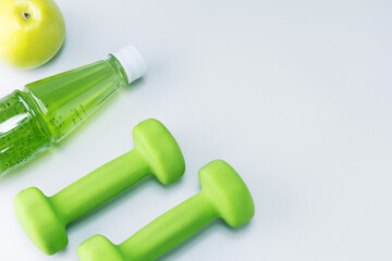 Fototapeta premium Dumbbells, fresh fruit apple and multivitamin juice on light grey surface with copy space. Healthy sport and diet concept.