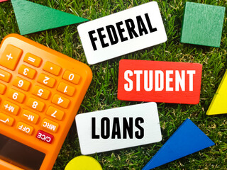 Colorful wooden board with calculator and text FEDERAL STUDENT LOANS on grass background.
