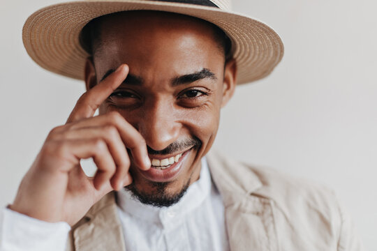 Guy in beige outfit is cute smiling on isolated background. Happy man in white shirt and beige hat looking into camera and laughing on white backdrop