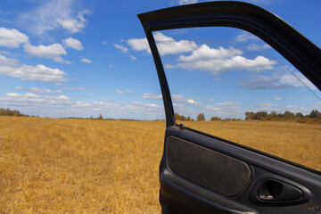 View of the yellow field and the blue sky with clouds from the open car door.