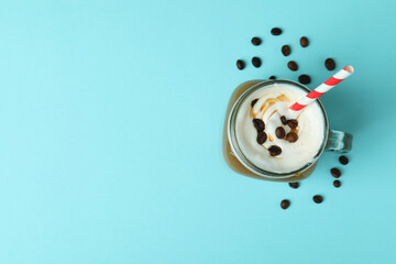 Glass jar of ice coffee and beans on blue background