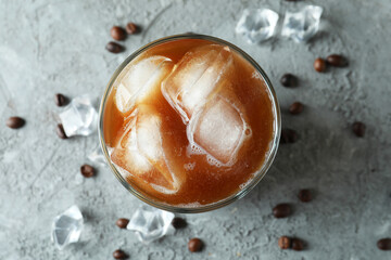 Glass of ice coffee, beans and ice on grey textured table