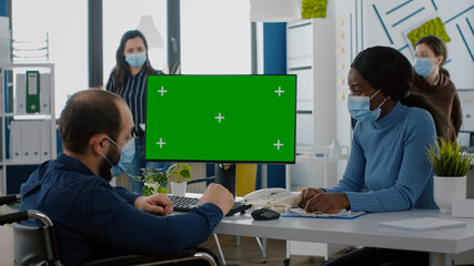 Handicapped invalid manager with protection mask sitting in wheelchair looking at desktop with...
