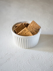 Natural flat rye mini-breads of a square shape in a white bowl on a light concrete background. Delicious and quick snack for dietary meals