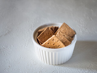 Natural flat rye mini-breads of a square shape in a white bowl on a light concrete background. Delicious and quick snack for dietary meals