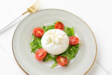 Salad with burrata cheese and cherry tomatoes on white wooden background