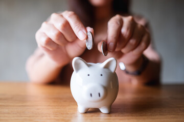 Obraz na płótnie Canvas Closeup image of a woman putting coins into piggy bank for saving money concept