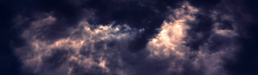Dramatic dark clouds on the sky with flaming red and orange areas in wide format