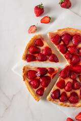 Homemade strawberry custard tart decorated with strawberry on marble background. Top view with...