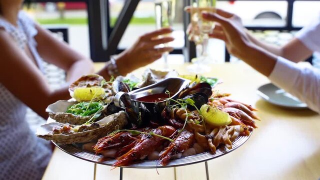 Mixed seafood salver, lobster shrimp, king prawns, mussels, oysters and squids are served for luxury restaurant visitors clinking glasses with wine and cheering. Traditional meditarian dish on tray.