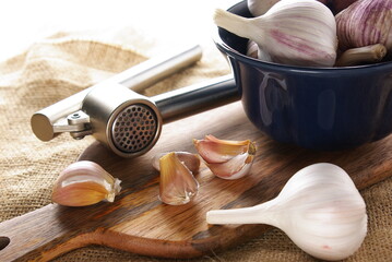 Garlic, garlic cloves and garlic press on a wooden board on a light background