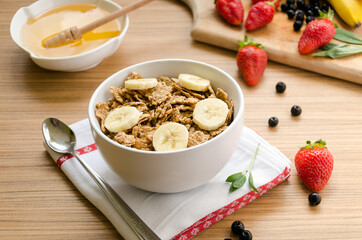 Healthy breakfast with bowl of cereals (muesli), strawberry, wild berries, honey and banana on light wooden table.
